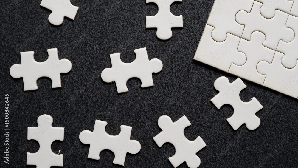 Obraz premium “Scattered white jigsaw puzzle pieces on black leather textured background. Concept image representing problem solving, decision making, strategic planning, missing piece, teamwork, or confusion.”