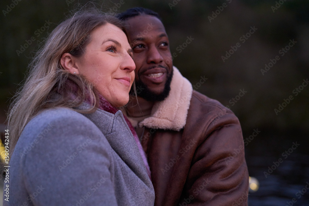 Fototapeta premium Smiling couple in warm clothing embracing outdoors at dusk