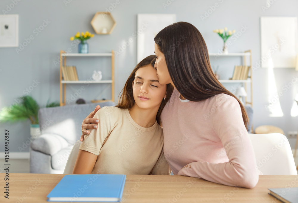 Young cheerful happy mother hugging and kissing her teen school girl daughter sitting at desk at home tired from school homework. Woman support child in studying. Education concept. Young cheerful happy mother hugging and kissing her teen school girl daughter sitting at desk at home tired from school homework. Woman support child in studying. Education concept.