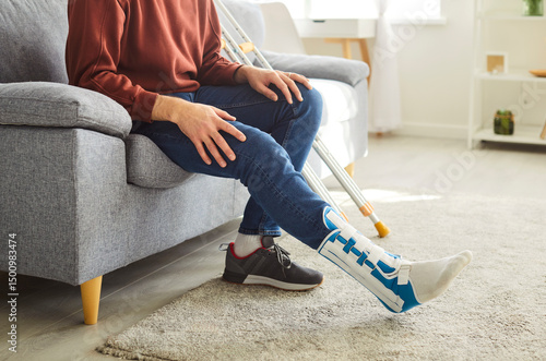 Obraz na plátně Unrecognizable faceless man with broken leg in plaster cast, posing on comfortab