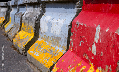 Fototapeta Naklejka Na Ścianę i Meble -  Red, grey and yellow painted concrete blocks with traces of use and weathering. Barriers used on the streets of french capital Paris at construction sites or events. Colorful row of some blocks.