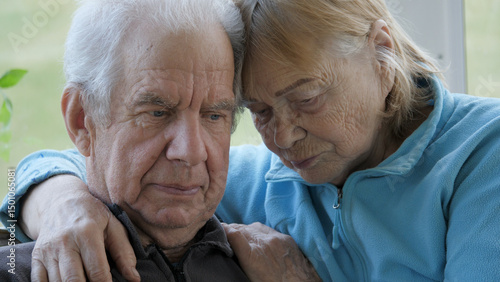 Elder old couple together hugging and with sad look silently looking down in nursing home. Lonely people without care and attention at home. Support and helping hand. Face with wrinkles and gray hair