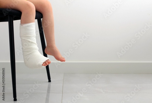 Child with broken leg sitting on chair  with a cast on leg.Close up of injured child leg in a modern interior during daytime