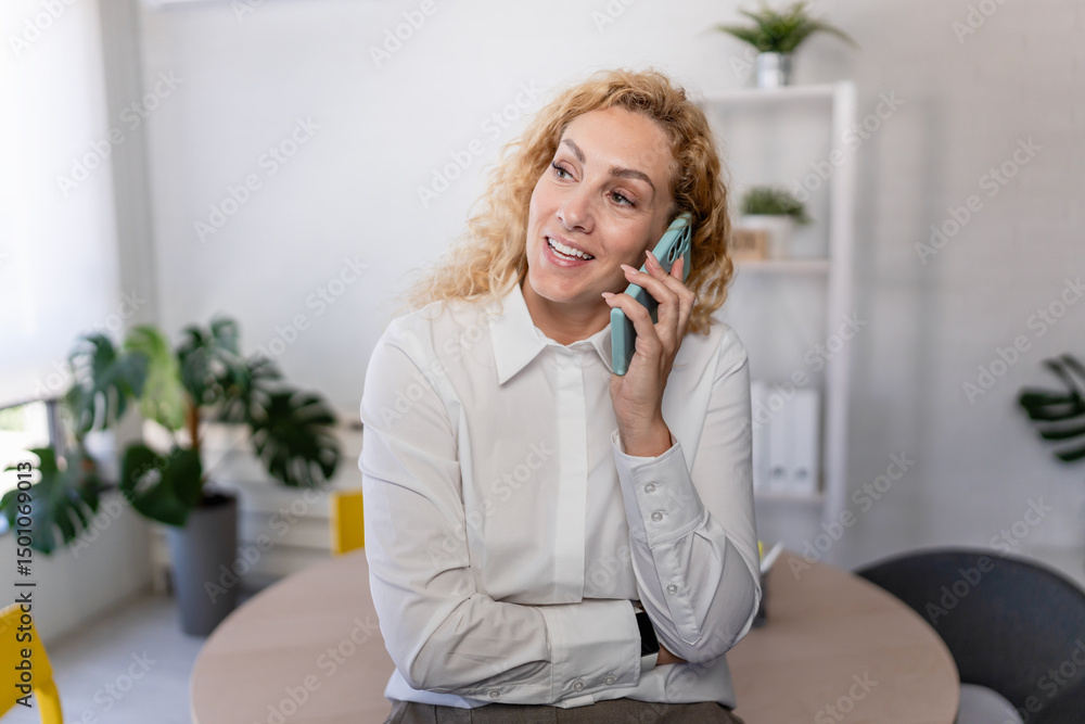 Smiling businesswoman talking on the phone in a modern office, standing confidently by her desk, engaged in a pleasant and professional conversation. Smiling businesswoman talking on the phone in a modern office, standing confidently by her desk, engaged in a pleasant and professional conversation.