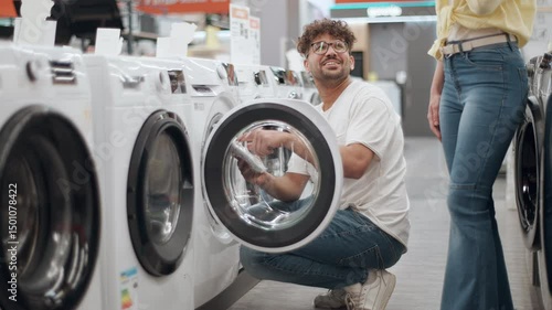 Happy couple choosing washing machine in electronics store. Young couple browsing home appliance store, comparing washing machine features with cheerful interaction.