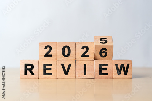 Turning wooden cube from Review 2025 to Review 2026. Concept of business review, new year planning, and annual reflection on gray background.