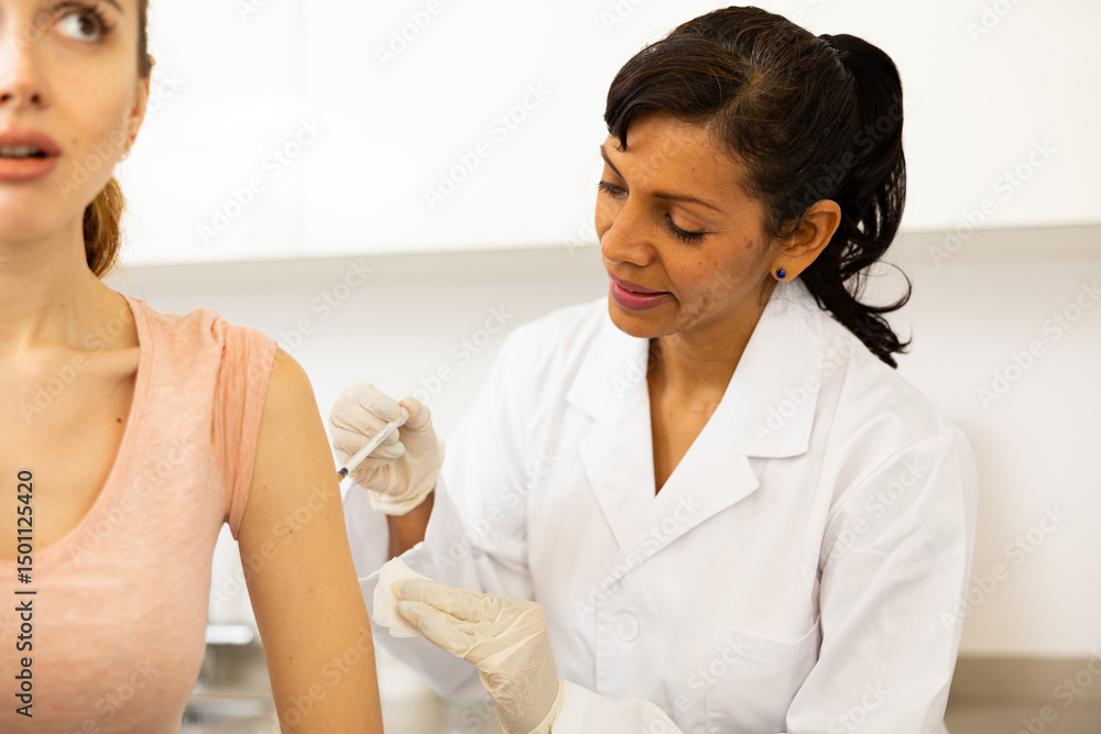 Obraz premium Portrait of positive woman doctor injecting shot of vaccine to female patient at clinic
