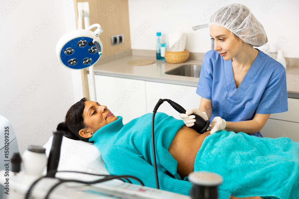 Obraz premium Young adult woman receiving radio frequency abdomen lifting procedure in cosmetology clinic