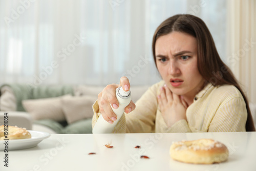 Tableau sur toile Emotional young woman spraying insecticide onto cockroaches at white table indoors, selective focus