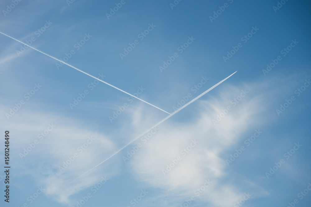 Airplane contrails intersecting in a beautiful blue sky with some cirrus clouds, creating an X shape Airplane contrails intersecting in a beautiful blue sky with some cirrus clouds, creating an X shape