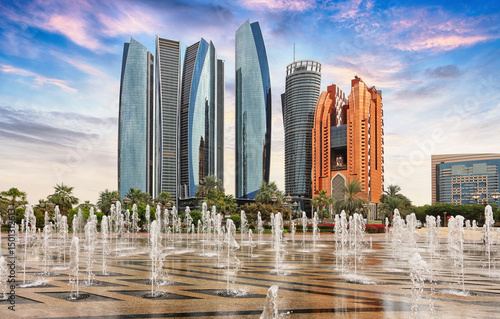 Skyscrapers in Abu Dhabi at dramatic sunset with fountain; United Arab Emirates
