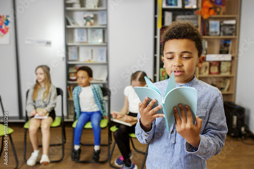 Young boy reads a book aloud during classroom activity in cozy learning environment. Back to school