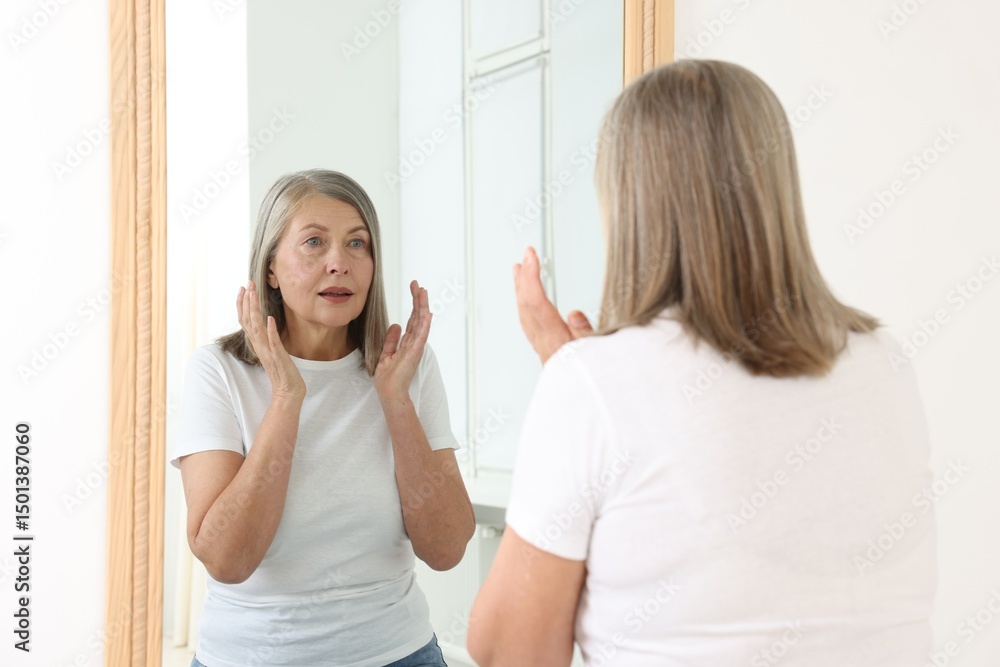 Fototapeta premium Beautiful senior woman looking at herself in mirror indoors