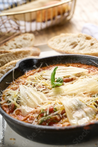 Shakshuka with baked eggs in tomato sauce, topped with melted cheese and basil, served hot in a cast iron skillet with rustic bread on the side.