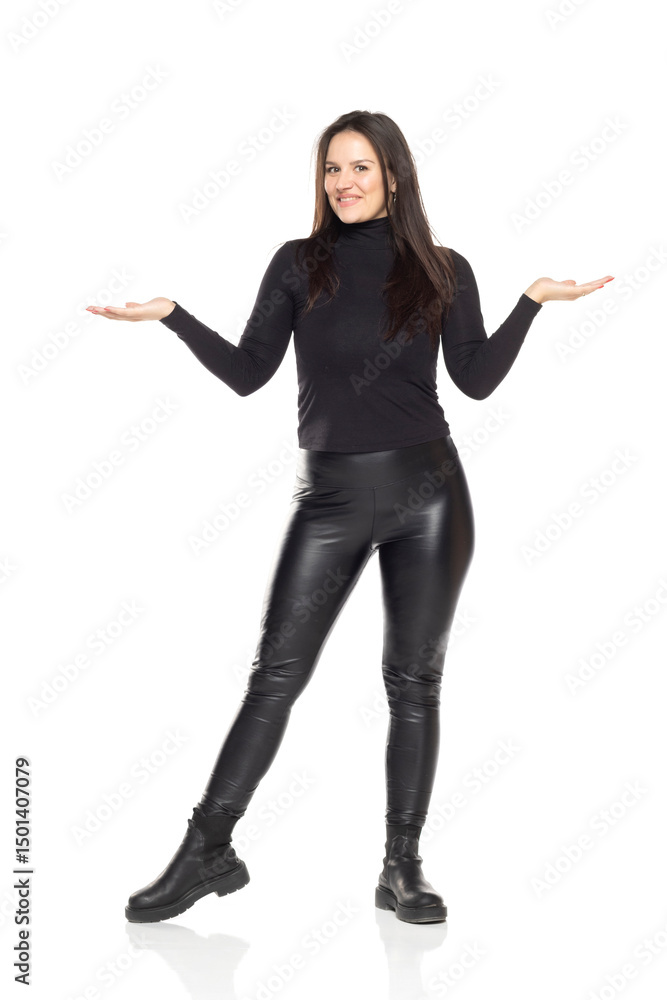 Studio shot on white background of smiling woman in black turtleneck and leather pants shrugging with open arms. Studio shot on white background of smiling woman in black turtleneck and leather pants shrugging with open arms.