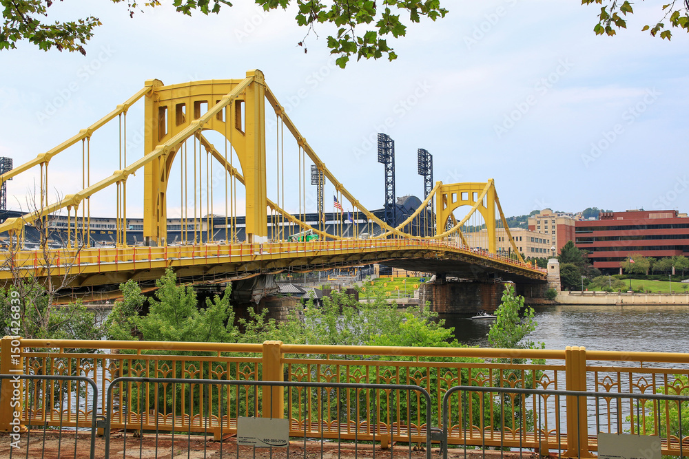 Obraz premium Captivating View of the Yellow Bridge Over the River in Pittsburgh with the Pirates Baseball Stadium in the Background