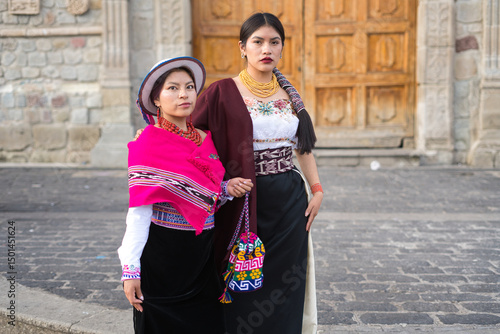 Two ecuadorian women wearing traditional andean clothing are posing together in front of a colonial church