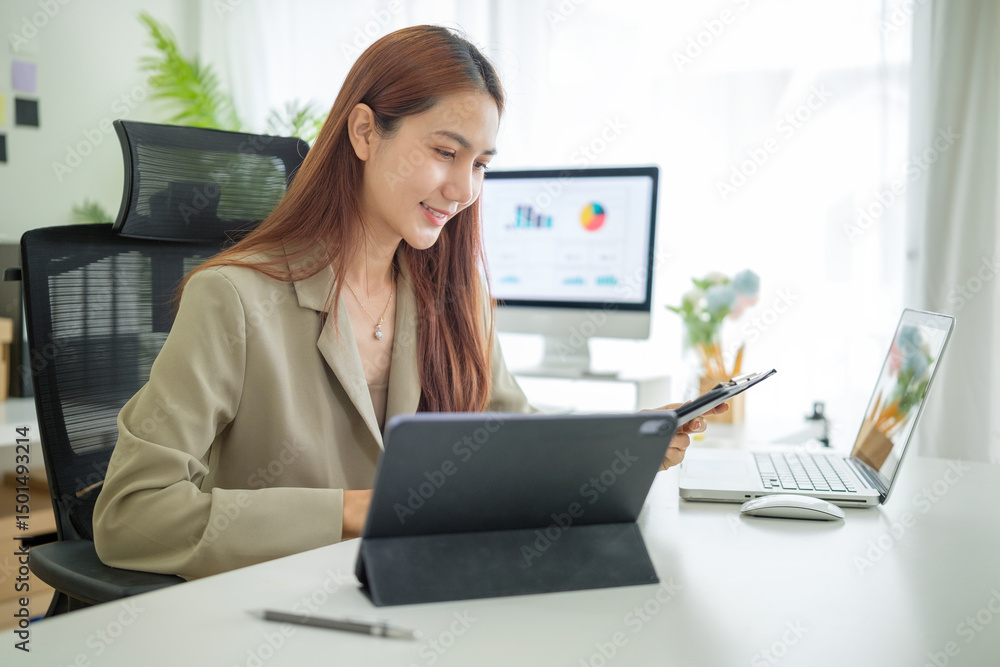 Young businesswoman reviewing documents on a clipboard while working in a modern office. Young businesswoman reviewing documents on a clipboard while working in a modern office.