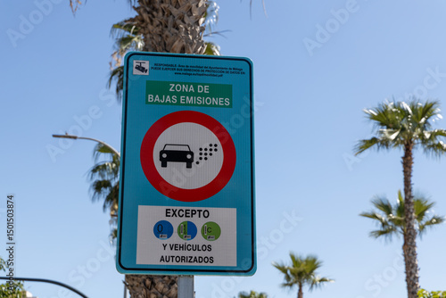 Emission zone sign indicating low emissions area with vehicle restrictions, surrounded by palm trees and clear blue sky, emphasizing environmental awareness and urban regulations