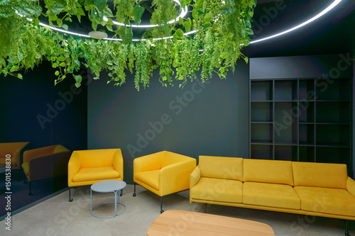 modern lounge area with vibrant yellow sofas and lush hanging plants creating a fresh and inviting atmosphere. sleek dark walls contrast with bright furniture in cozy office setting