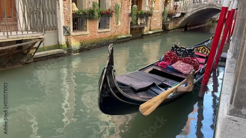 Empty venetian gondola floating on narrow canal with calm water and historic brick buildings

