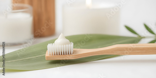 A bamboo toothbrush holds a dollop of white organic toothpaste beside a soft green leaf