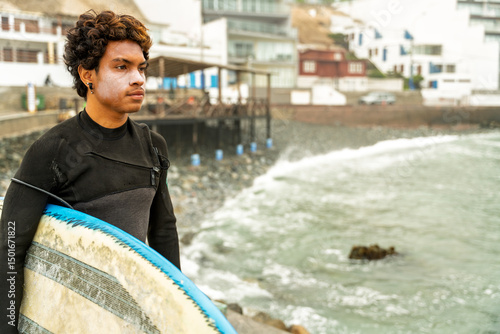 Surfer wearing sunscreen entering ocean by breakwater in coastal town