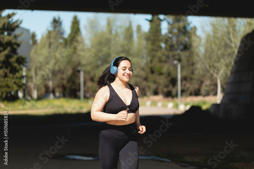 A strong young woman plays sports and runs in the park happy, listening to music with headphones