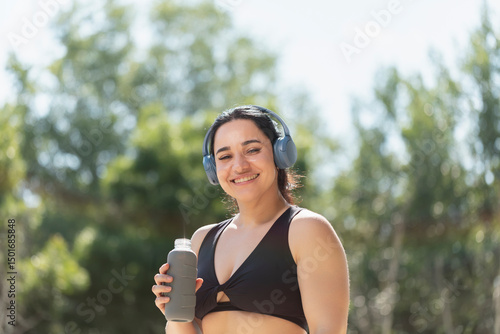A young girl smiles while drinks water to hydrate herself, from a reusable bottle, during a morning exercise session