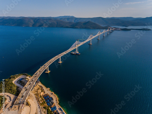 Aerial view of peljesac bridge construction site over clear water with scenic mountains in the background, Komarna, Croatia.