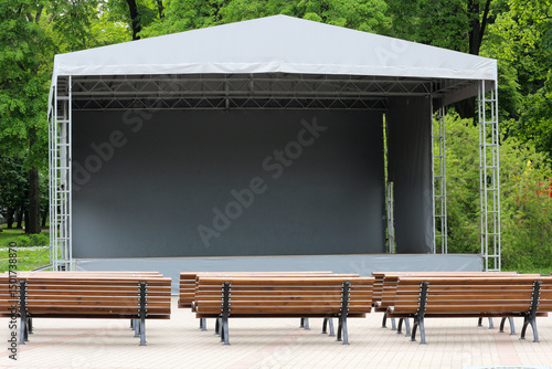 Portable mobile stage with tent cover and aluminum frame with Wooden Benches in Park Setting