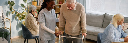 Senior man using walker being assisted by nurse in elderly care facility
