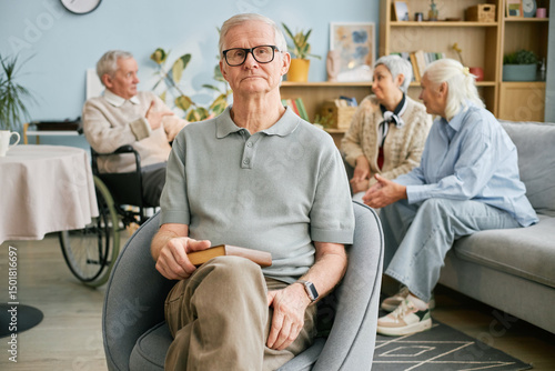 Photography Portrait of elderly man sitting comfortably in chair, holding book in hand while