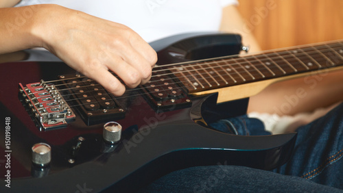 Close-up of a women playing a guitar on a bed. Guitar strings visible. Relaxed atmosphere with an emphasis on music. A woman plays an electric guitar.