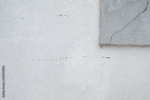 Cracked Stucco Wall: Close up of a textured white stucco wall with cracks and a gray concrete corner showcasing aging and structural details