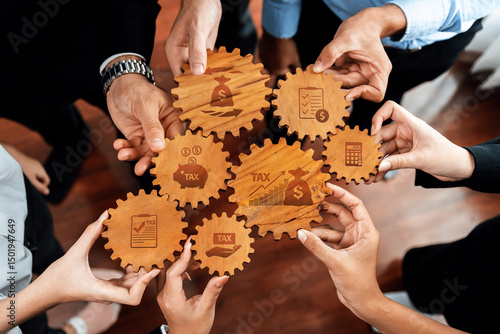 This image portrays hands collaborating around wooden gears, each representing various financial concepts like tax and budgeting, highlighting teamwork and strategic planning. Amity