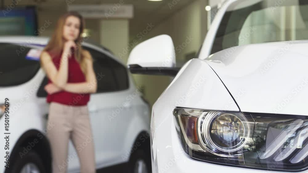 Female customer thoughtfully examining a sleek new car at the dealership Female customer thoughtfully examining a sleek new car at the dealership