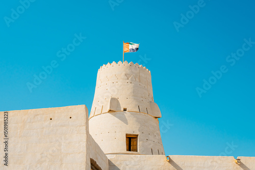 Stone arabic watchtower with waving United Arab Emirates National Flag in Al Jazirah Al Hamra haunted town in Ras Al Khaimah. High quality photo