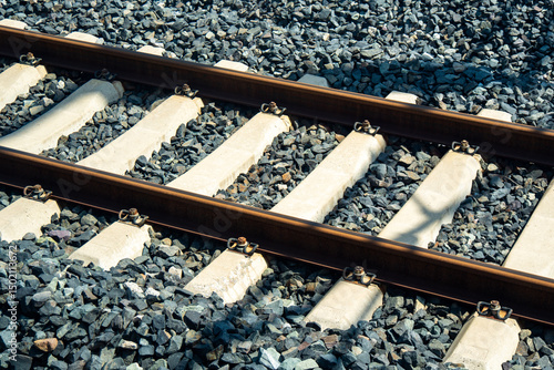 This image, reflecting a transportation concept, shows a close-up of modern railroad tracks with concrete sleepers embedded in dark ballast.