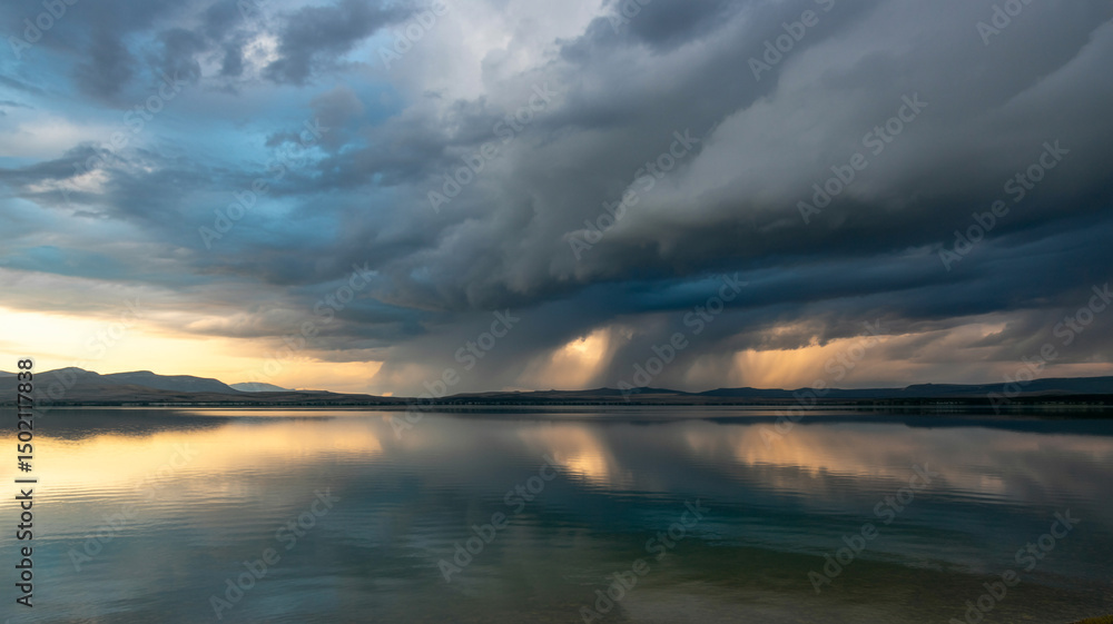 Obraz premium Dramatic sunset storm clouds over calm lake and mountains