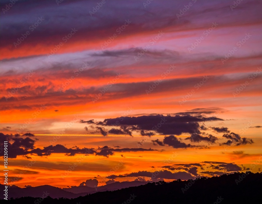 Fototapeta premium Fiery Sunset Over Silhouetted Mountains with Dramatic Cloud Form