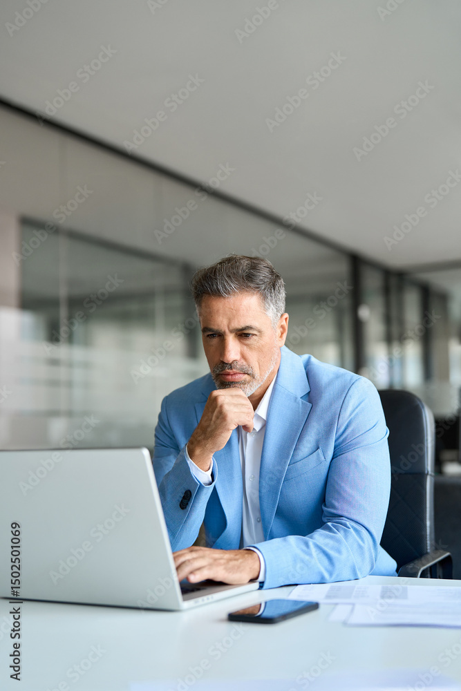 Busy middle aged professional business man financial investor, 50 year old senior businessman executive in suit using laptop computer working on investment project sitting at office desk. Vertical. Busy middle aged professional business man financial investor, 50 year old senior businessman executive in suit using laptop computer working on investment project sitting at office desk. Vertical.