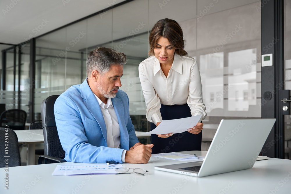 Obraz premium Two busy professionals man and woman business leaders of middle age checking accounting documents financial report talking working together on laptop computer in office at corporate meeting.