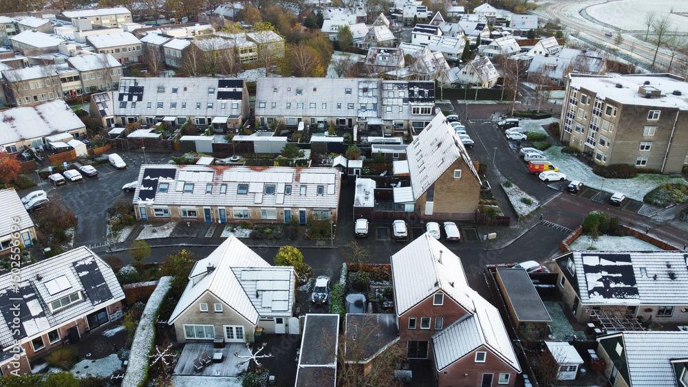 Fototapeta premium Houses with solar panels snow on roof during winter. Drone shot of street in a residential area neighborhood in The Netherlands.