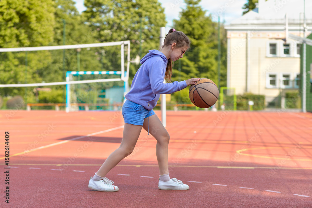 Fototapeta premium Teenage girl playing basketball on the playground. Children and sports.