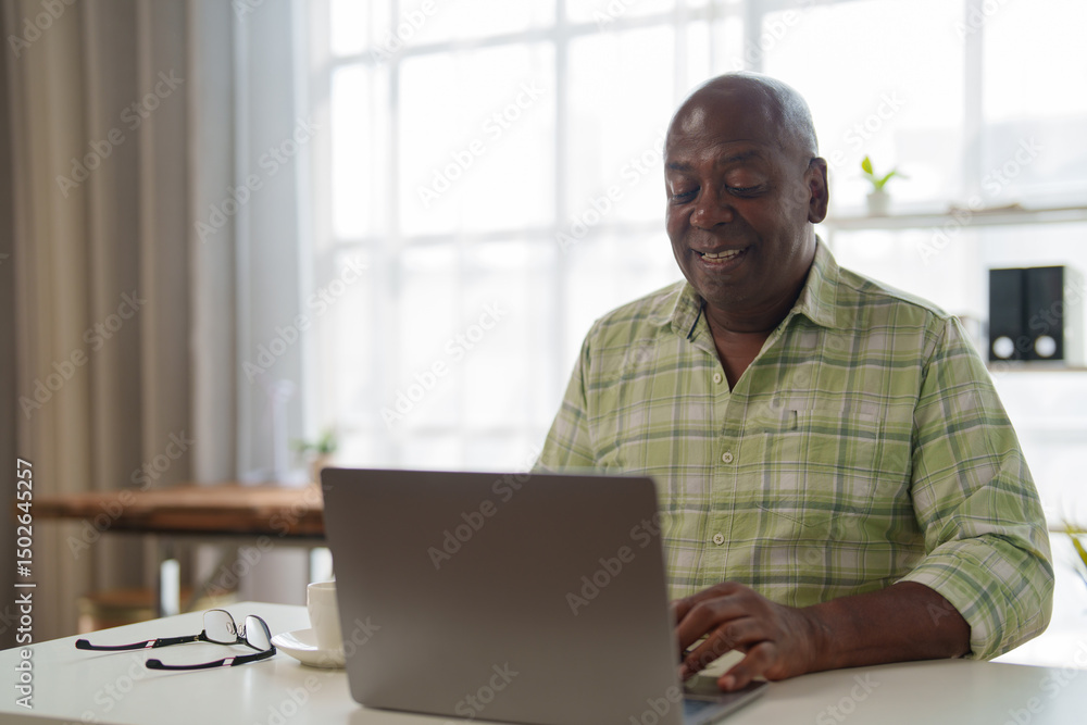 Fototapeta premium Happy african american businessman using laptop computer, working from home office, typing on keyboard, smiling, modern workspace, bright window light