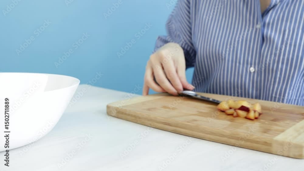 Woman adds sliced nectarine to bowl of fruit on blue background, fruit preparation for breakfast or dessert, modern kitchen with a focus on fresh nutrition. Woman adds sliced nectarine to bowl of fruit on blue background, fruit preparation for breakfast or dessert, modern kitchen with a focus on fresh nutrition.