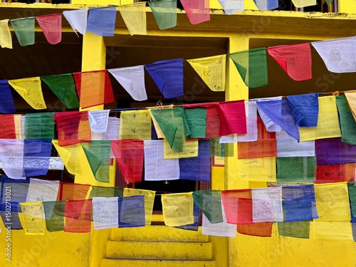 Colorful Tibetan prayer flags outside the Nano Buddha stupa with a wall of yellow pain in the background