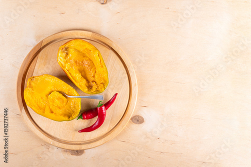 Top view of two halves of mango, two red hot chili peppers and spoon on wooden background with copy space