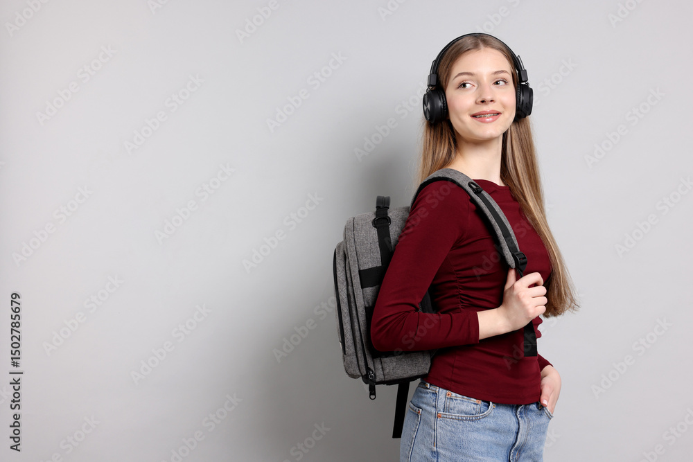 Teenage girl with headphones and backpack on light grey background. Space for text Teenage girl with headphones and backpack on light grey background. Space for text